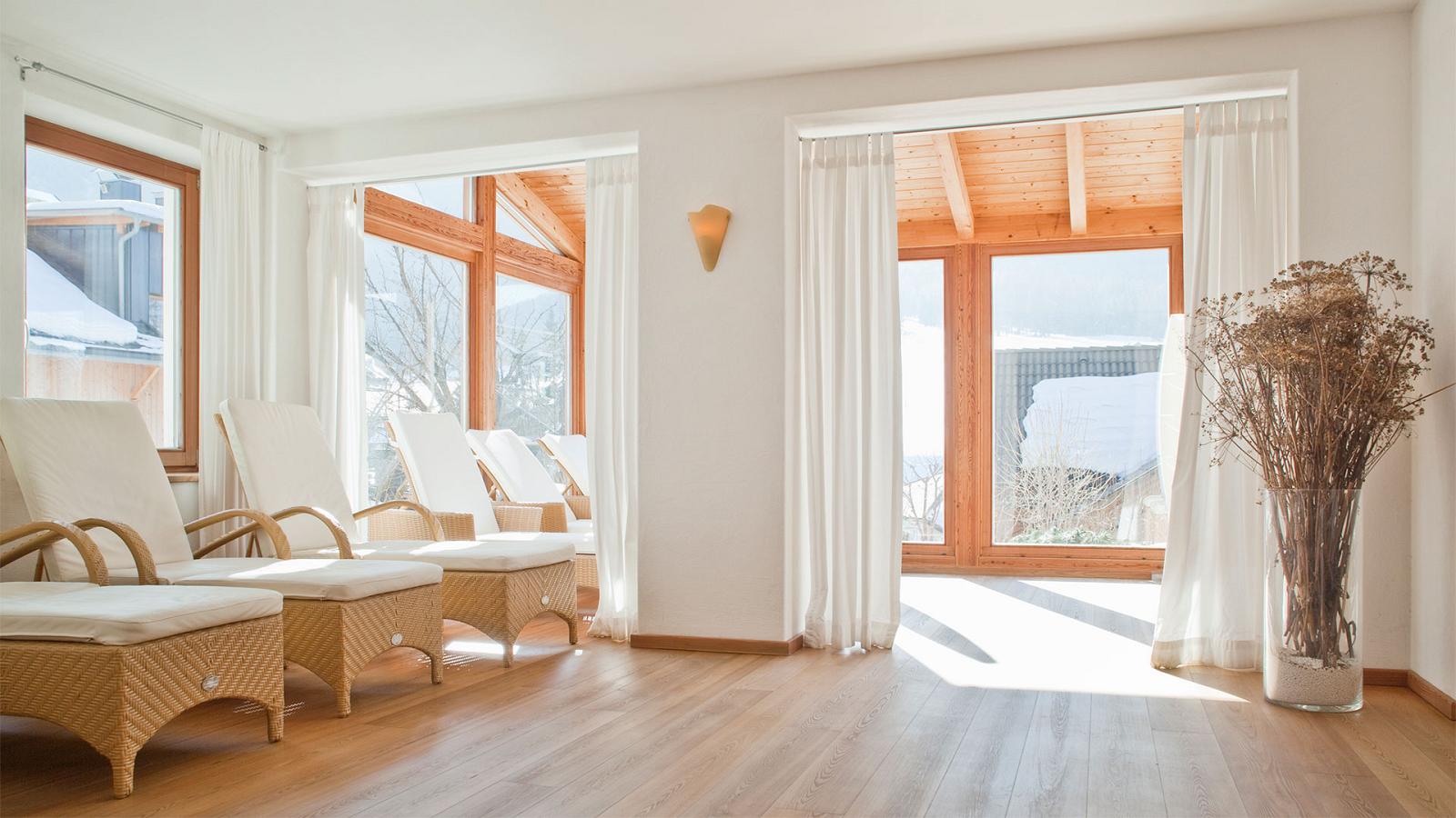 Der elegante Wellnessbereich des Hotels Strobl mit aufgereihten Liegebetten, weißen Gardinen und großen Fenstern