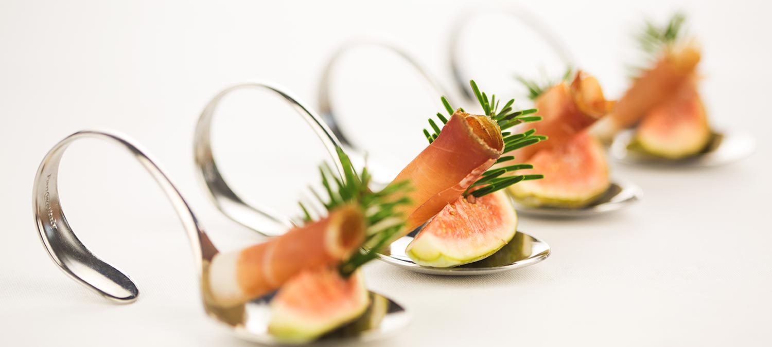 Tasty fingerfood composed of fresh fig, a slice of South Tyrolean speck and sprig of spruce, served on a special silver spoon