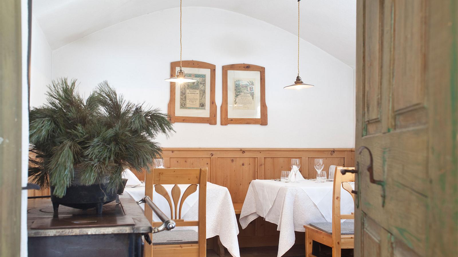 Eine Ecke des Speisesaals des Hotel Strobl in Sexten mit Holzmöbeln, antiken Gemälden, Latschenzweigen über einem Holzofen und zwei elegant dekorierten Tischen