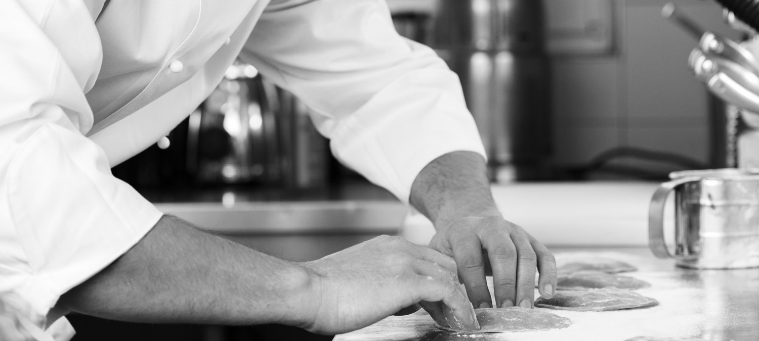 Dettaglio sulle mani del nostro chef che impastano con la farina alcuni ravioloni