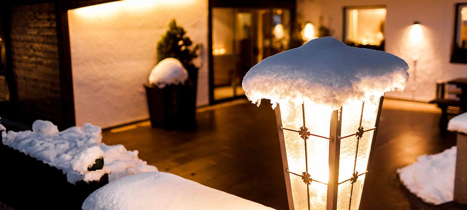 Detailansicht einer verschneiten Schmiedeeisenlampe vor dem Hotel Strobl