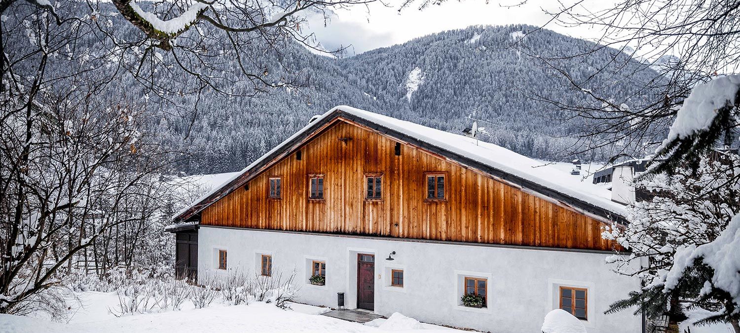 Ein typisches Haus in Sexten im Pustertal im Winter, mit schneebedeckten Bergen und Wäldern im Hintergrund